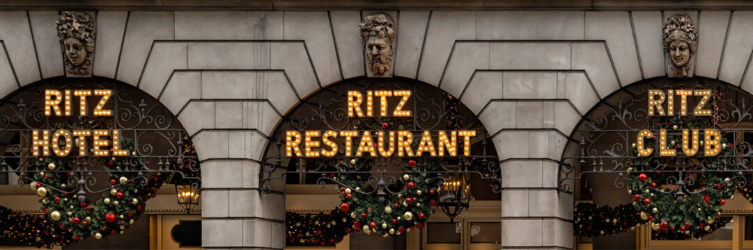 LONDON, UK - NOVEMBER 16, 2022:      Panorama vit of lit signs for Ritz Hotel, Ritz Restaurant and Ritz Club outside the Ritz building on Piccadilly, Mayfair