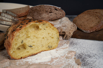 Different types of sliced bread and a loaf on a wooden background . Spilled flour. Front view. Copy space. A half cut loaf . Fresh crusty bread.