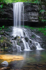 Beautiful waterfall during spring with silver colored water, cascading down the cliff covered by green plants - 550123585