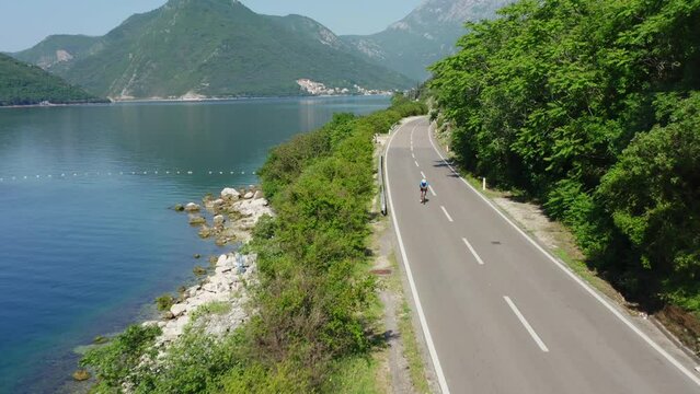 Cycling race - cyclists one the sea coast road, aerial view. Fly over athletes. Summer sunny day. mountain landscape around