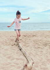 Pretty girl balancing on a thick branch lying at the beach