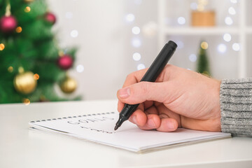 Man writes marker board at white table with Christmas decor goals and plans new year and Christmas....