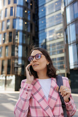 Fototapeta premium successful business woman in a pink jacket and glasses goes to the office to work and talks on the phone. the top manager is an entrepreneur, a happy confident woman smiles. business marketing and