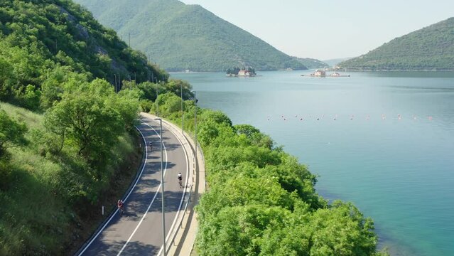 Coast road with a cyclists in Kotor bay, Montenegro. Aerial view. Island on a background.