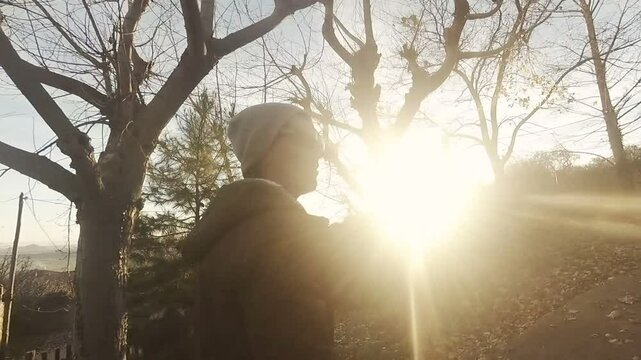 Hombre joven andando sonriente en paisaje de puesta de sol en invierno con niebla. Camino entre arboles secos y vegetacion.