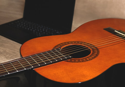 Classic acoustic orange guitar with a black laptop on a wood textured table. Online instruction