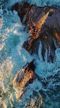Aerial top view of waves and rocks in the sea, slow motion. Vertical video