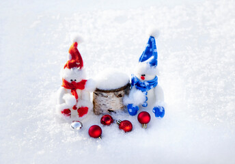 Two toy snowmen standing in the snow near red New Year's balls. The concept of the New Year and Christmas time