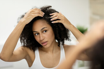 Portrait of a beautiful young woman examining her scalp and hair in front of the mirror, hair...