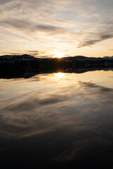 Dramatic sunset. View of the sun hiding in the horizon and beautiful twilight sky with clouds reflection in the lake's water surface.  