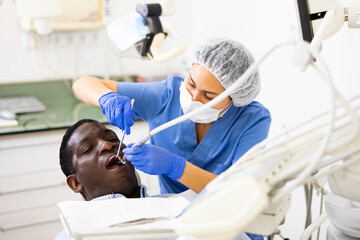 Dentist is treating male patient which is sitting in dental chair