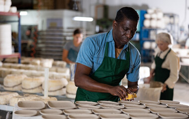 African-american man potter in apron polishing new crafted plates with sponge.