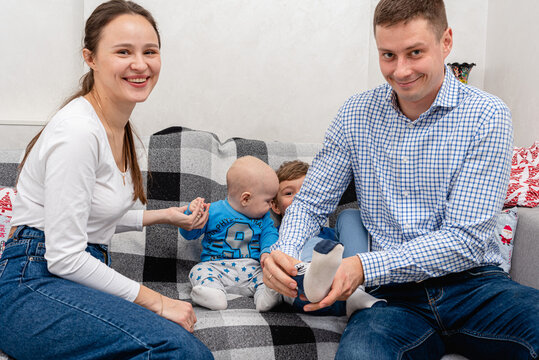 A young, emotional, cheerful, big family, mom, dad and sons are sitting on a big bed, putting on a sock for their son, smiling. Preparing for shooting. - Powered by Adobe