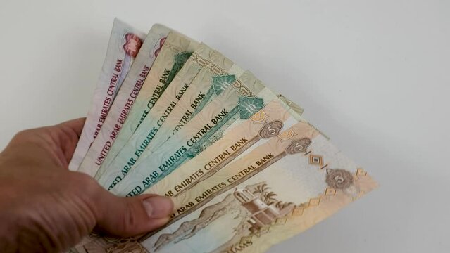 Hand counting United Arab Emirates dirhams on white background.