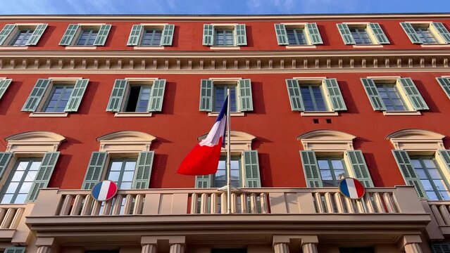 the flag of France waves on the classical facade of the building at sunset