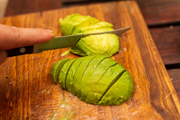 person cutting an avocado into slices on a board