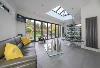 Interior of beautiful house in winter showing Christmas tree in stylish designer room with garden and patio seen through bifold doors.