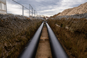Two large metal pipes with a plastic sheath laid in a trench. - obrazy, fototapety, plakaty