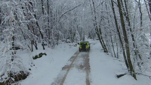 MARCH 2022, LJUBLJANA, SLOVENIA: AERIAL: Beautiful winter drive with Jimny Suzuki 4x4 car through snowy forest. Mini 4-wheel SUV vehicle moving through woodland along snow-covered road on cloudy day.