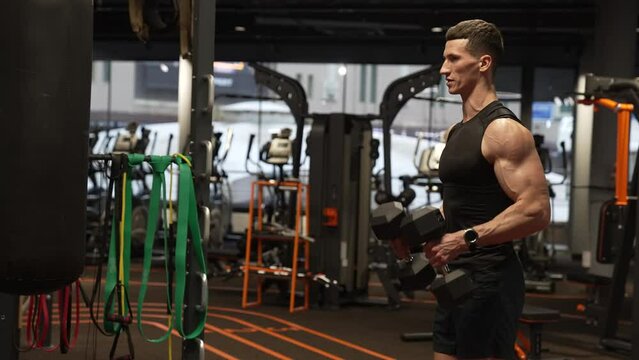 Athlete exercising with dumbbells in indoor gym. Fit man doing biceps triceps curls workout in gym