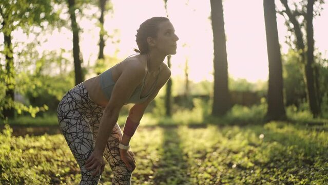 Young athletic woman resting and taking a deep breath after a training in the forest. Healthy lifestyle concept. Slow motion. 