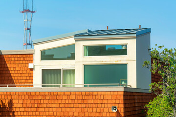 stucco and wood slatted house with folliage and sutro tower background on blue sky midday in sun