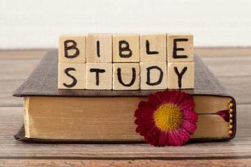 Bible study text on wood cubes, closed Holy Bible Book with golden pages, and flower on rustic...
