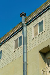 Beige stucco facade on side of house or building with vertical metal chimney pipe with nearby windows and white accent color