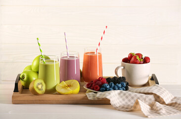 Glasses of different tasty smoothies and fresh ingredients on white wooden table