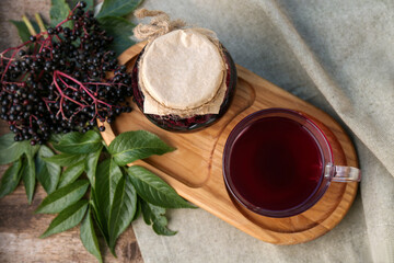Fototapeta na wymiar Elderberry jam, glass cup of tea and Sambucus berries on table, flat lay
