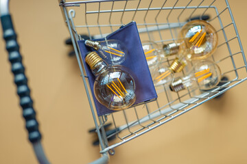 Purchase of electricity.lot of electric lamps in a shopping cart.Consumption and payment for energy consumption.Light bulbs in a supermarket trolley on a beige background.Crisis in the energy sector.