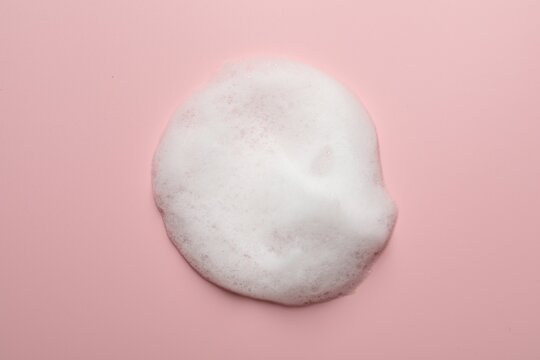 Drop of fluffy soap foam on pink background, top view