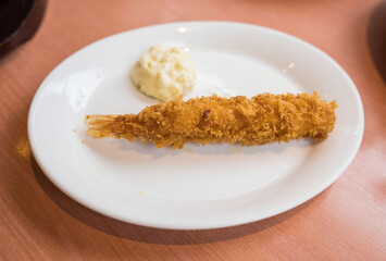 This image shows a beautifully plated tempura shrimp with a dollop of white sauce on the side.