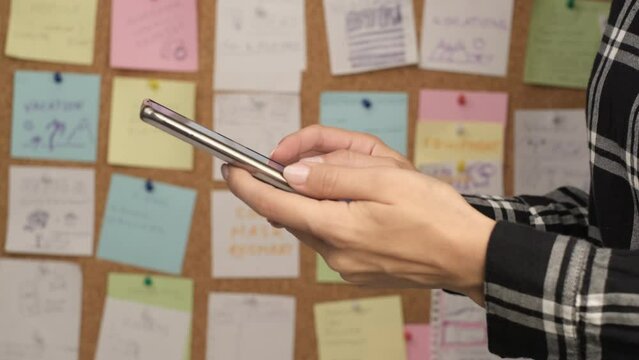 Using a smartphone for planning tasks and calendar events in the office, use of digital technologies to change a business model. Sticky notes on a cork board in the background. Selective focus