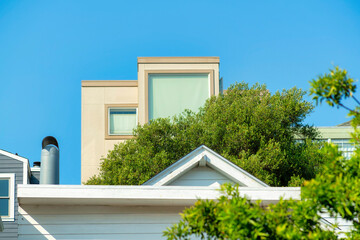 Hidden house tower with bright trees and smaller rooftops in midday sun with clear blue sky background.