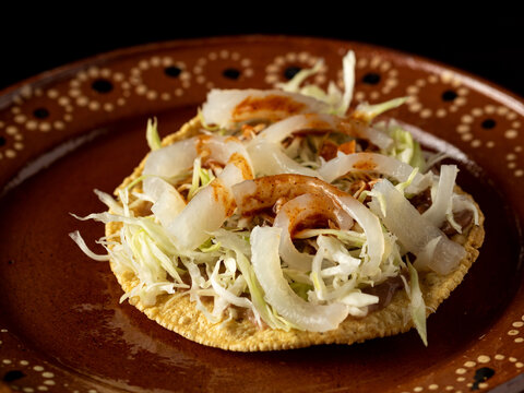 Tostada con repollo, crema, cueritos de cerdo y salsa.