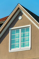 Double gable roof with brown stucco exterior with red brick roof tiles and window with white accent color
