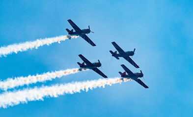 Silhouettes of training aircraft performing aerobatics on a clear sunny day.