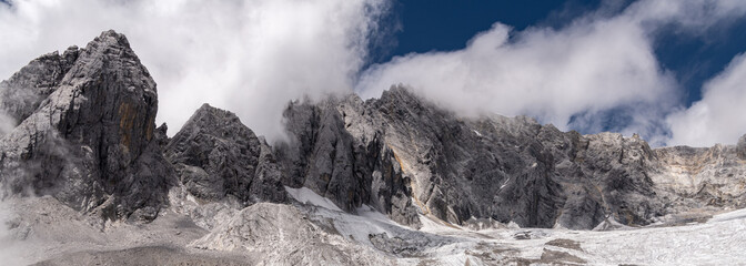 Fototapeta na wymiar Huge panorama of the Jade Dragon Snow Mountain with blue sky and epic white clouds. Landscape of beautiful nature of Jade Dragon Snow Mountain in China, Yunnan