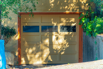 Beige garage door with three glass windows in mostly shade in late afternoon in front of house