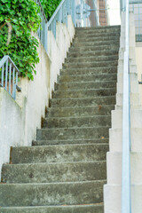 Long set of cement stairs with white stucco banister with metal hand rail and side foliage and plants