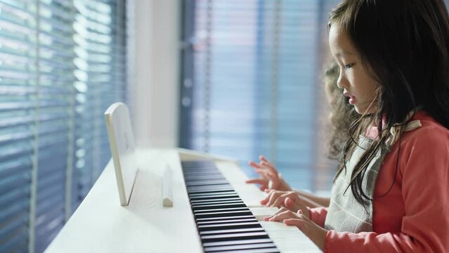 Two Asian adorable children enjoy playing piano in living room at home.