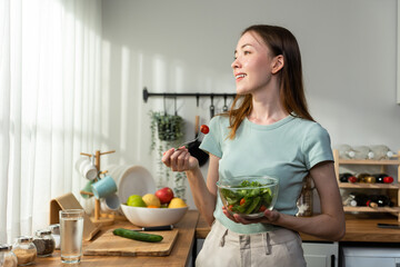 Caucasian young woman eating healthy green salad in kitchen at home.  