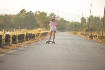 Teenager Beautiful happy Asian healthy woman smiling,riding and playing extreme sports skateboard as outdoor activity with happiness, relaxation during holidays in summer vacation at park morning time