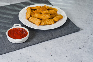 Fish sticks in a crunchy golden breading and bowl of ketchup close-upon the kitchen table