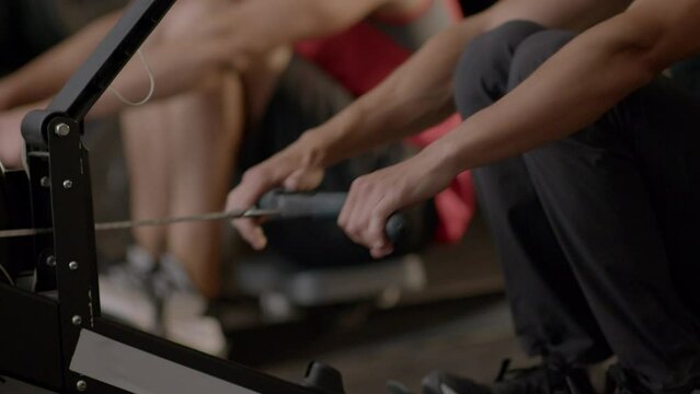 Close up of young athletes working out on rowing machine in the gym. Healthy lifestyle concept. Slow motion.