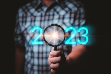 Male hand holding a magnifying glass With the number of the year 2023, it represents the search for new things in a new way