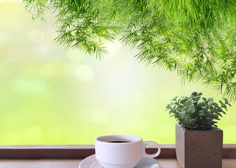 Green leaves of bamboo It is on top and the bokeh is visible. On the table there is a cup of coffee and small green leaves in pots on the wooden floor.