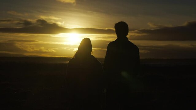 Silhouetted couple in love admiring beautiful sunset by sea, rising above grass