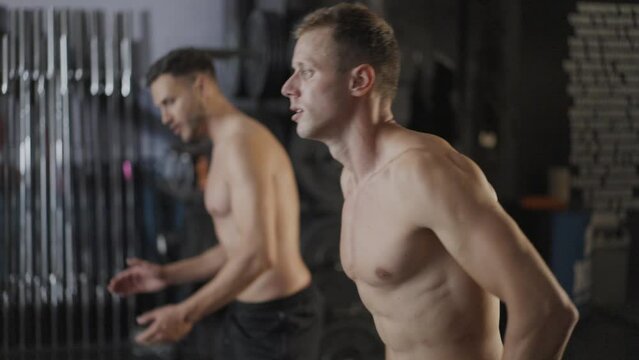 Two young shirtless men finishing a kettlebell high pull exercise. Healthy lifestyle concept. Slow motion.